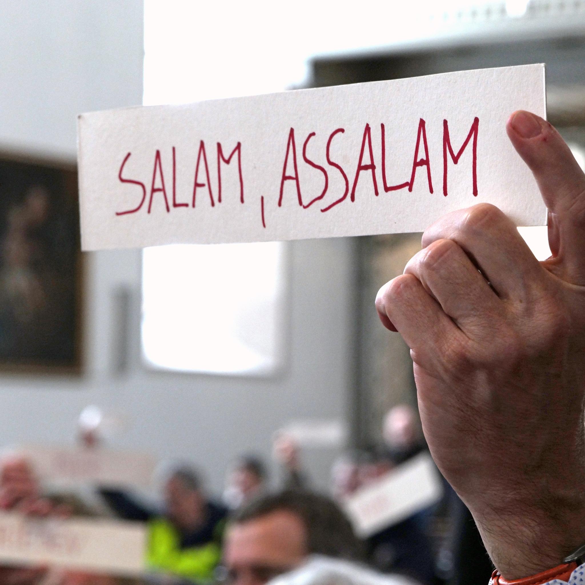Hand hält Schild mit der Aufschrift 'Salam, assalam'