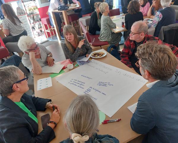 Menschen sitzen an Tischen und diskutieren.