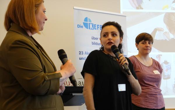 Drei Frauen stehen auf einer Bühne, zwei haben ein Mikrofon in der Hand.