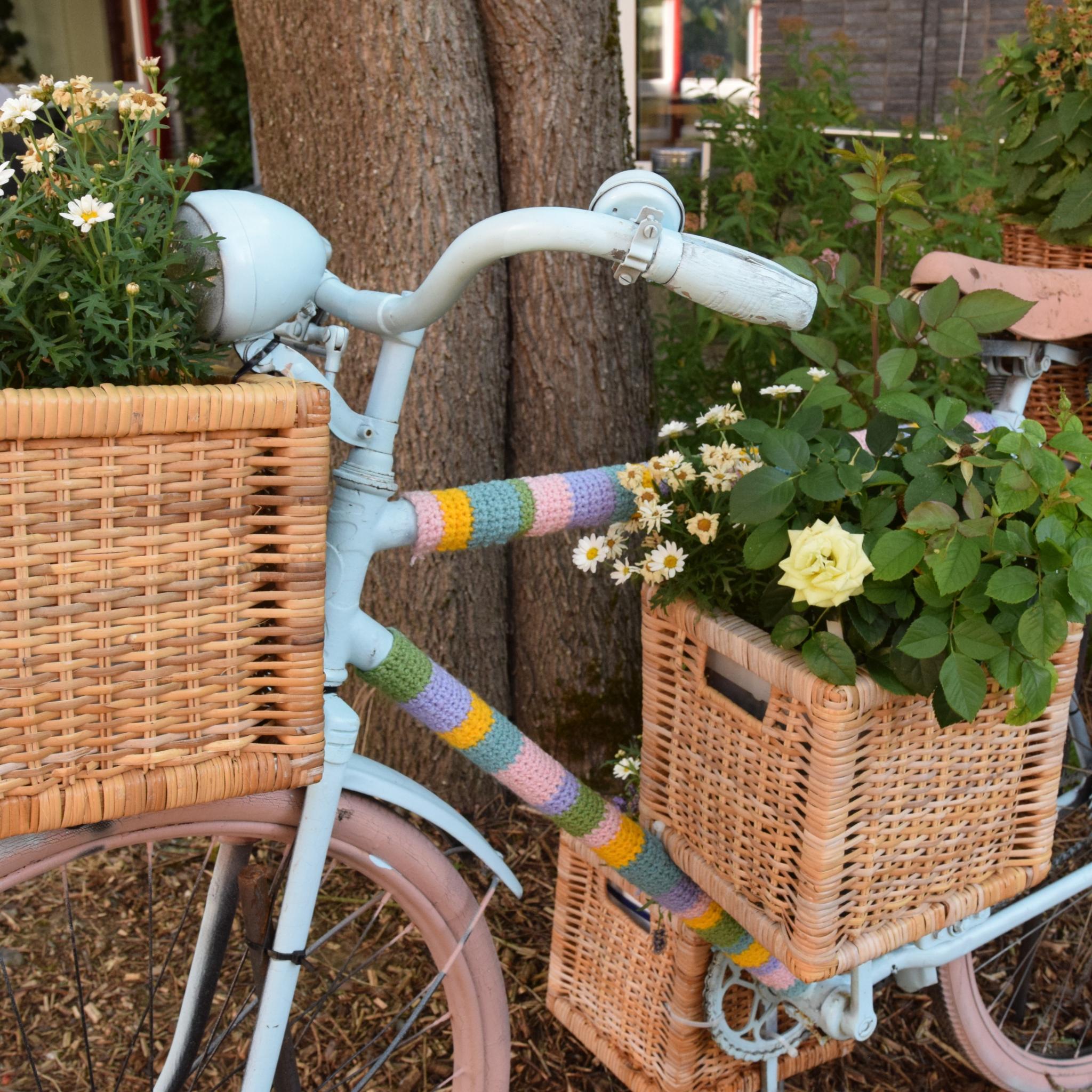 Ein Fahrrad ist mit bunter Wolle, Blumenkästen und Blumen verziert und lehnt an einen Baum.