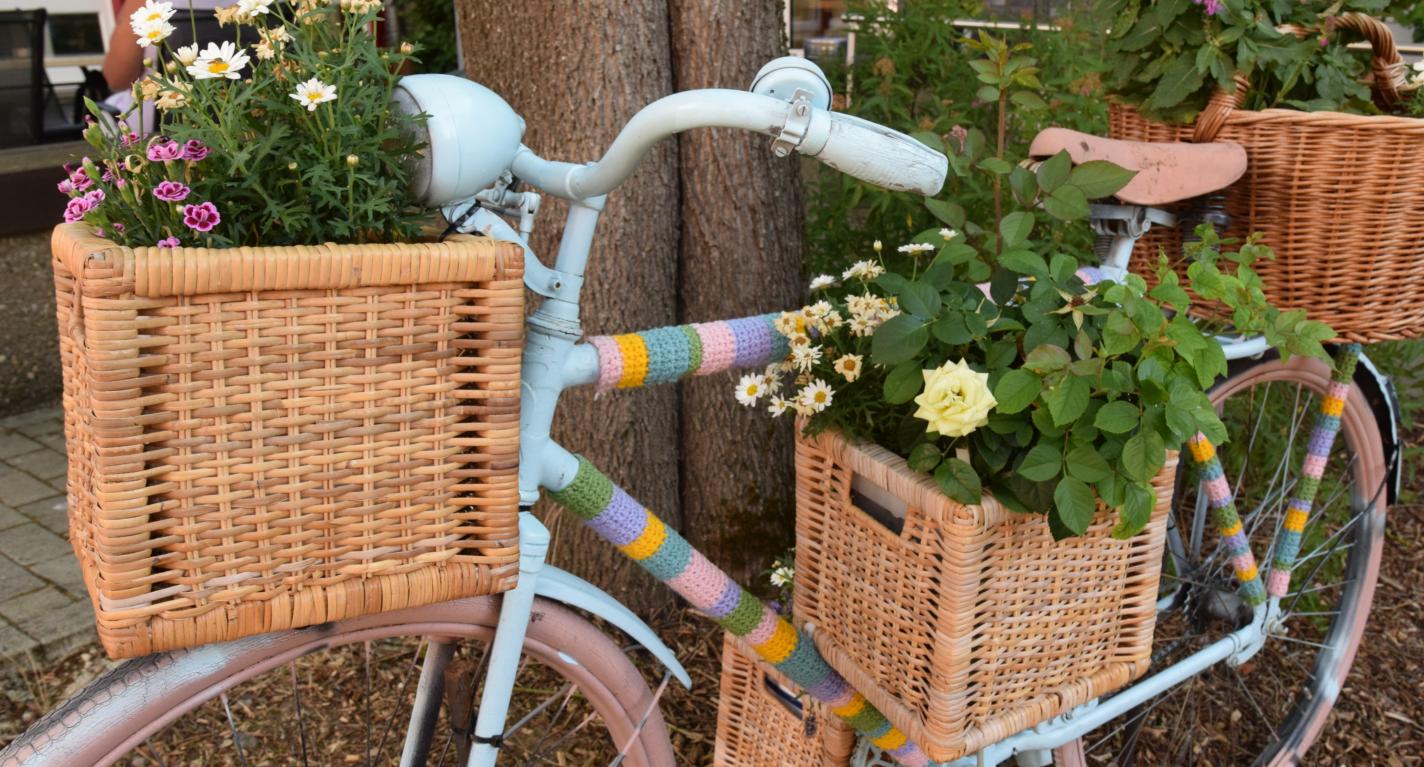 Ein Fahrrad ist mit bunter Wolle, Blumenkästen und Blumen verziert und lehnt an einen Baum.