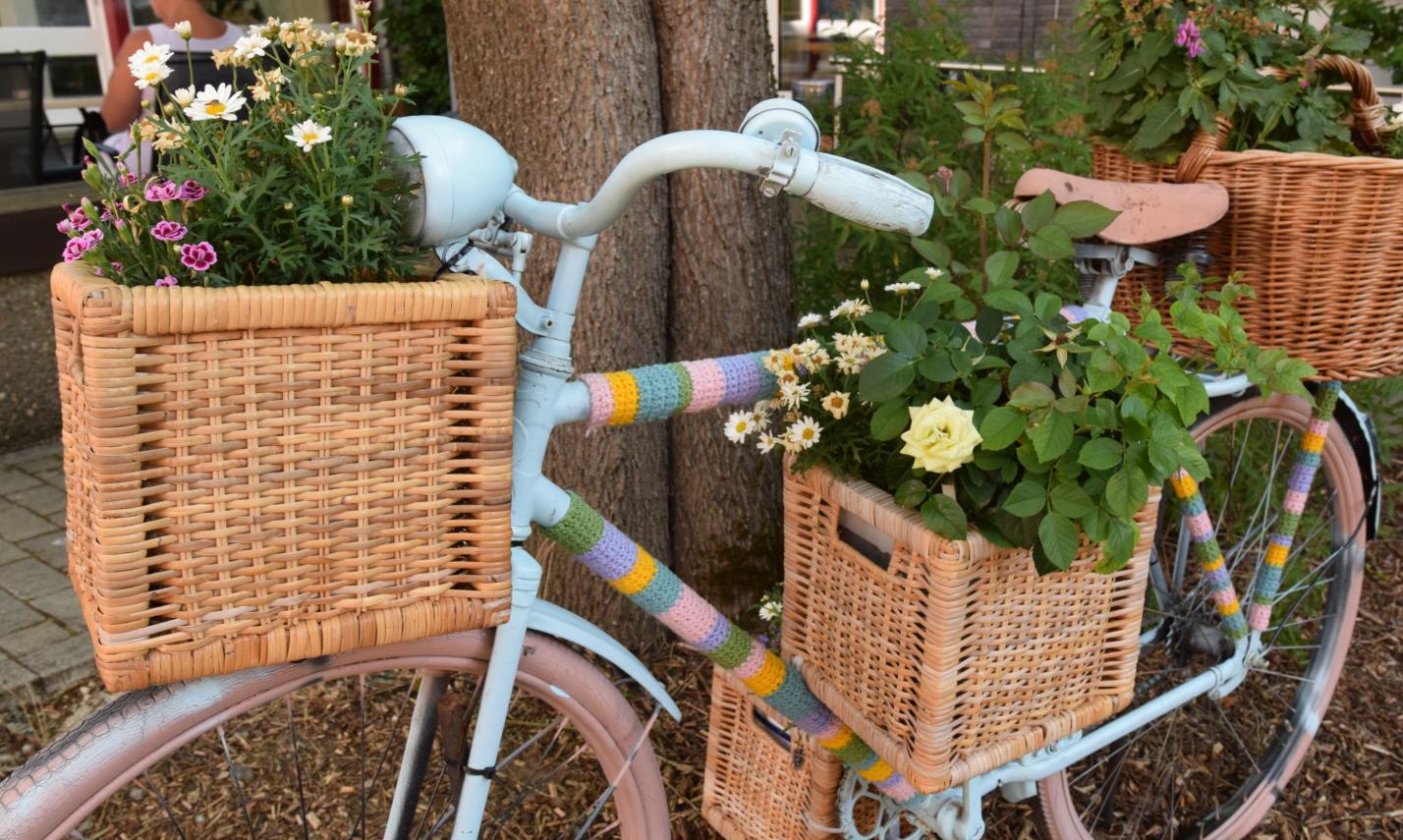 Ein Fahrrad ist mit bunter Wolle, Blumenkästen und Blumen verziert und lehnt an einen Baum.