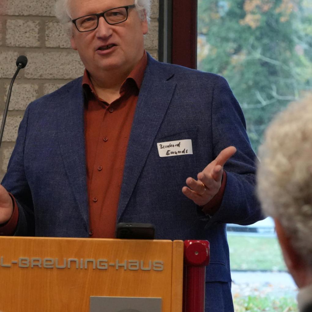 Ein Mann spricht am Rednerpult zu Menschen und hebt dabei die Hände.