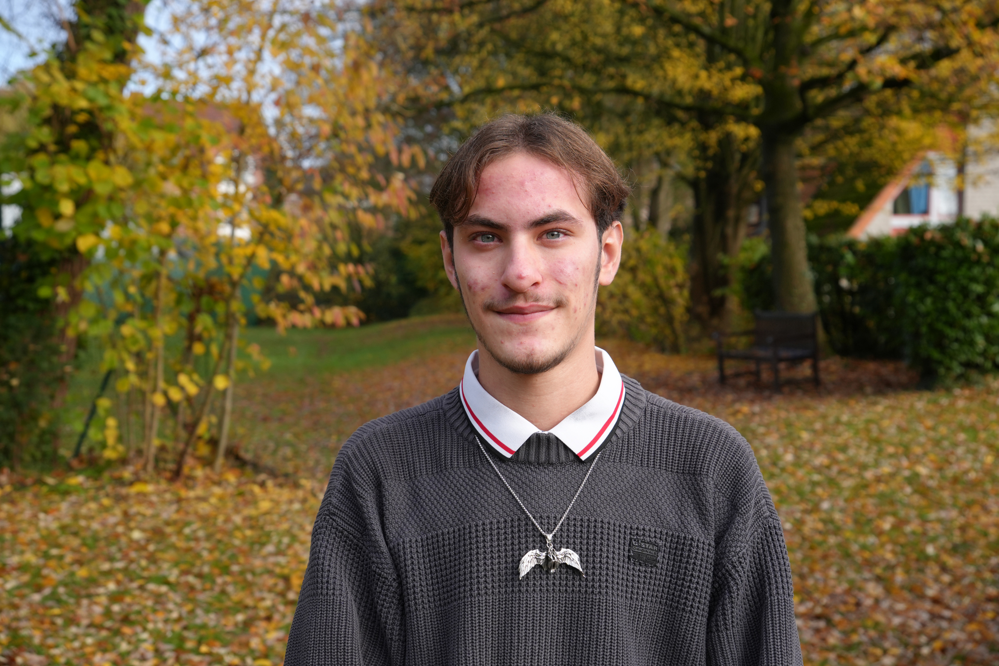 Junger Mann vor einem herbstlich gefärbtem Park.