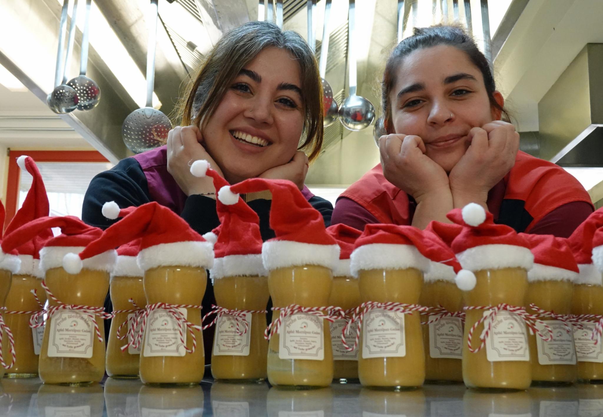 Zwei Frauen hinter einer Reihe von Marmeladengläsern mit Zipfelmützen.