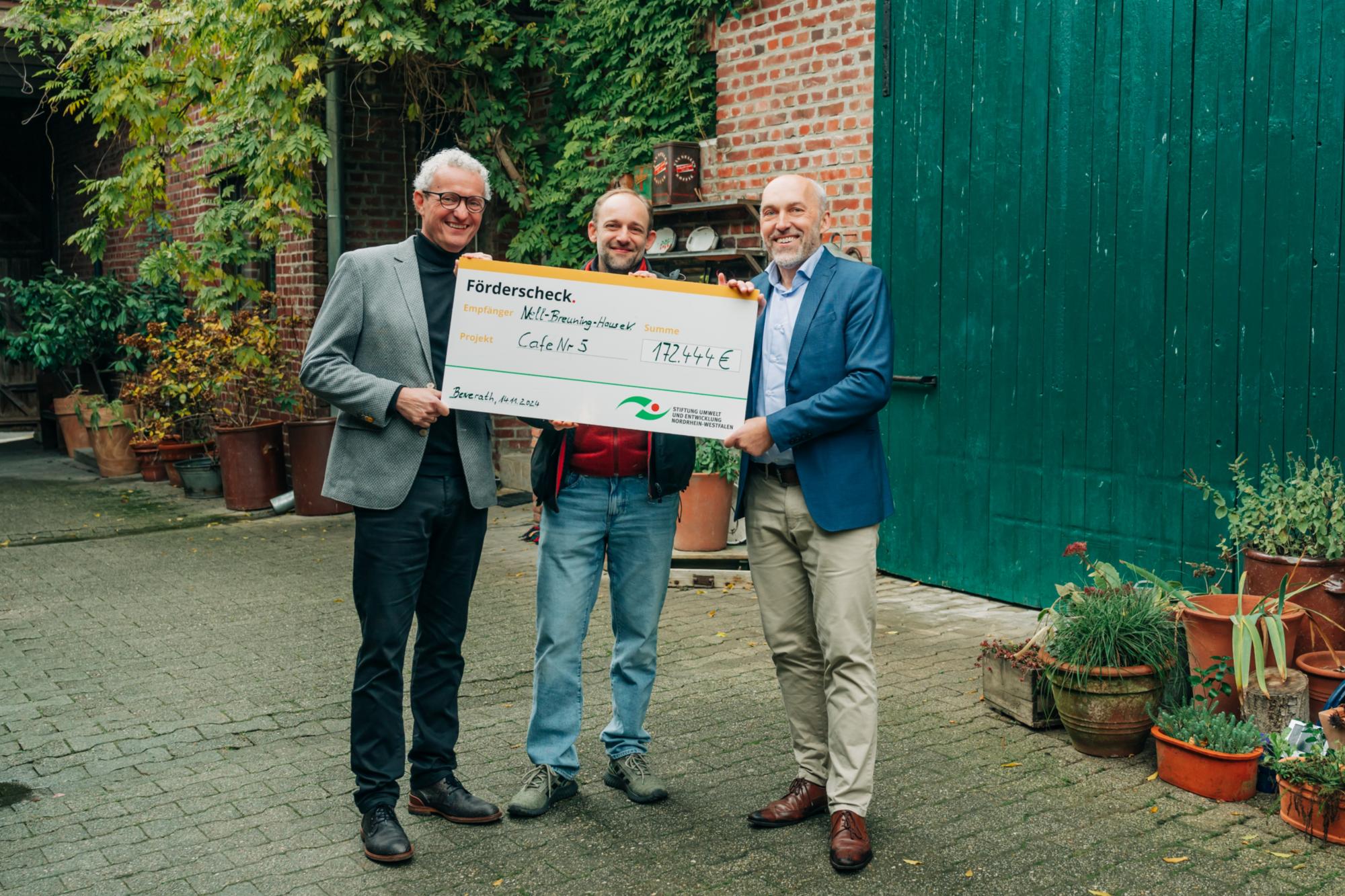 Dr. Manfred Körber (links) und Jonathan Querg (mitte) vom Nell-Breuning-Haus e.V. freuen sich über die Übergabe des symbolischen Förderschecks durch Frank Griesel von der Stiftung Umwelt und Entwicklung Nordrhein-Westfalen.