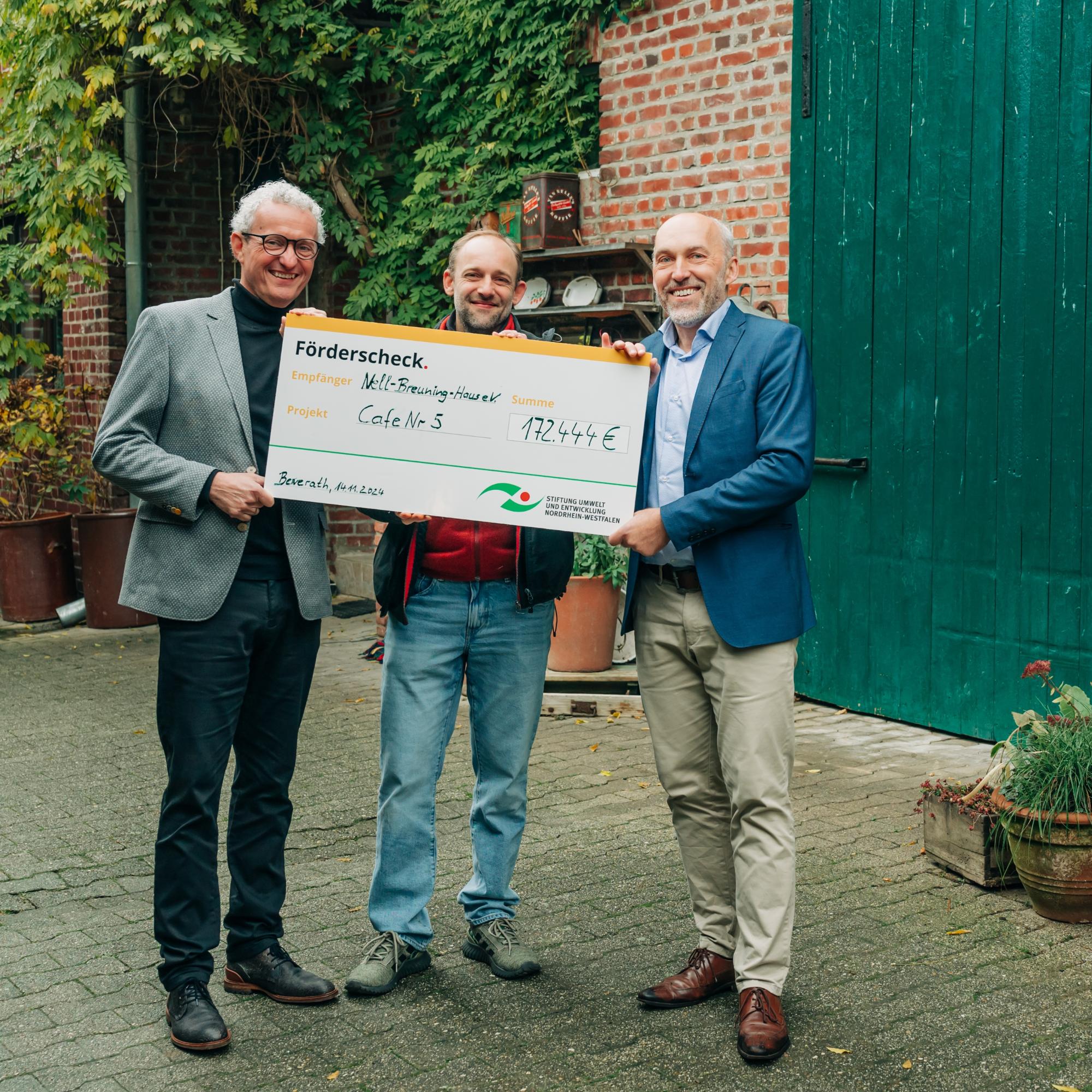 Dr. Manfred Körber (links) und Jonathan Querg (mitte) vom Nell-Breuning-Haus e.V. freuen sich über die Übergabe des symbolischen Förderschecks durch Frank Griesel von der Stiftung Umwelt und Entwicklung Nordrhein-Westfalen.