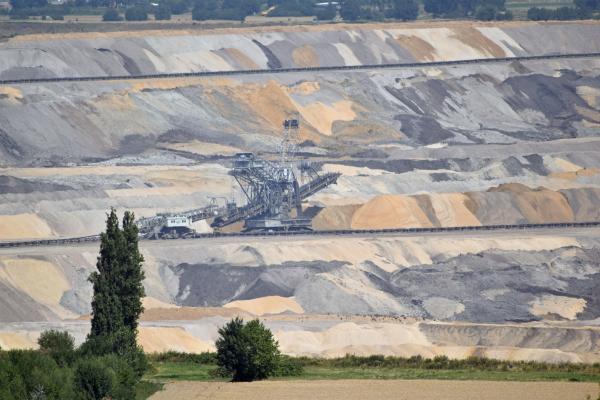 Ein Tagebau mit einem Bagger in den Flözen. Vorne noch Feld und Bäume.