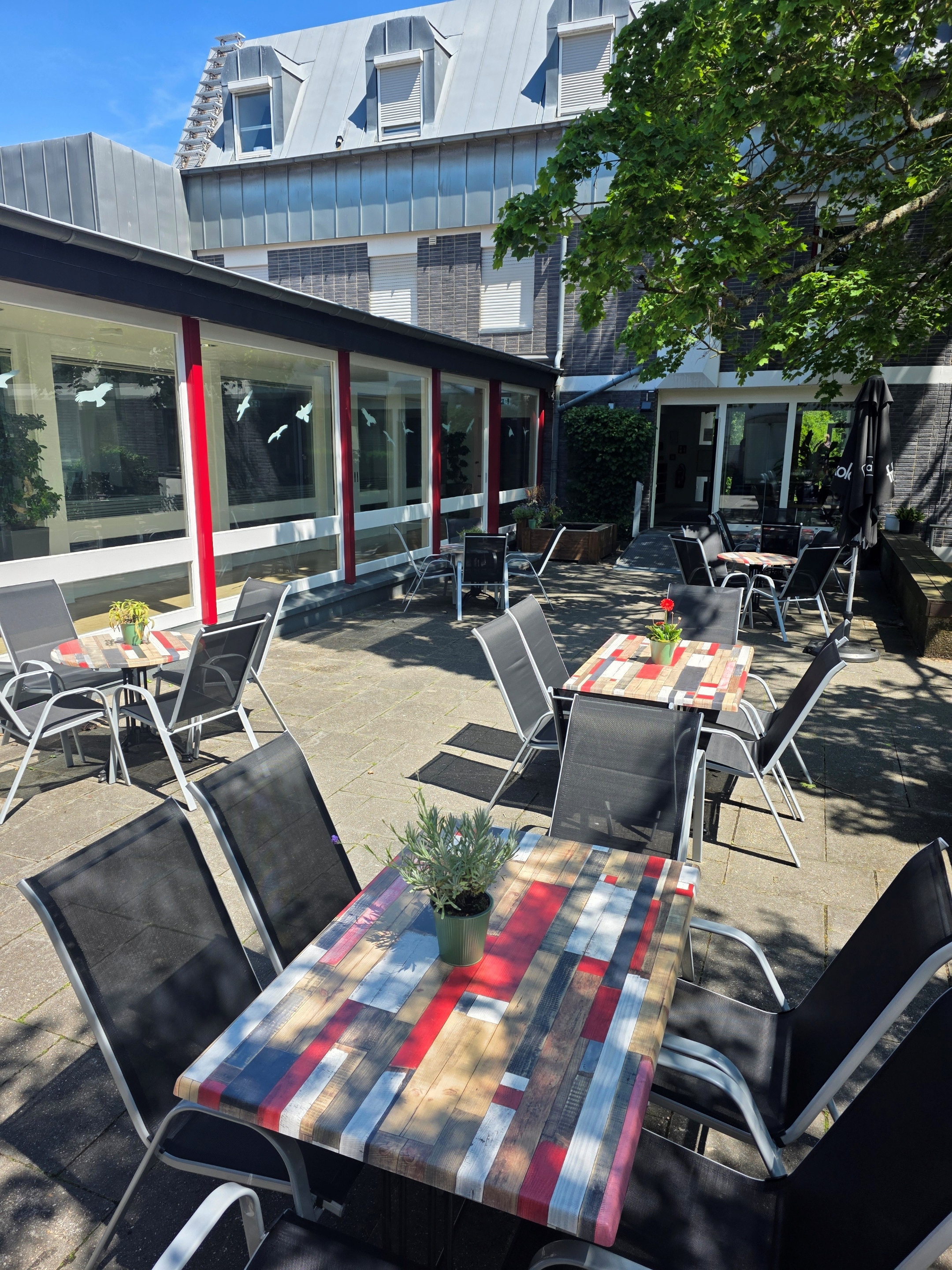 Auf einer Terrasse stehen für Sitzgruppen Tische mit farbigen Tischplatten.