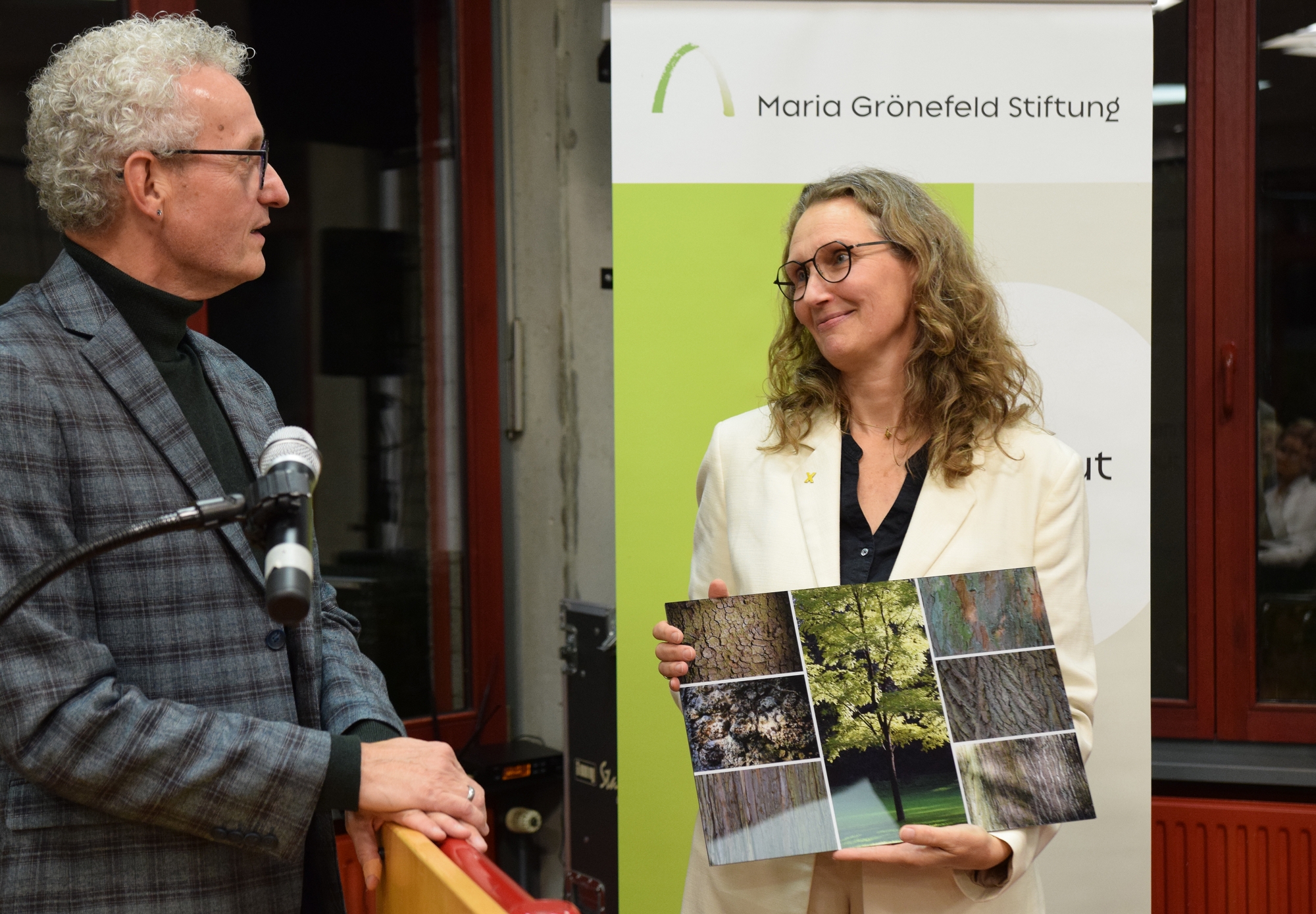 Antje Grothus bekam aus den Händen von Dr. Manfred Körber zunächst die offizielle Urkunde, in der ihr Eintreten für Klimagerechtigkeit gewürdigt wurde. Und dann erhielt sie eine kunstvolle Collage von Baumbildern des Aachener Fotografen Dieter Kaspari. (c) Thomas Hohenschue